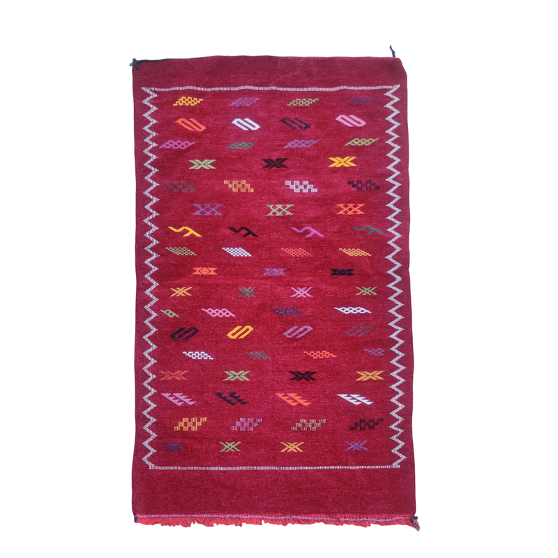 Tapis berbère bordeaux, fait main, avec motifs géométriques multicolores et bordure en zigzag.