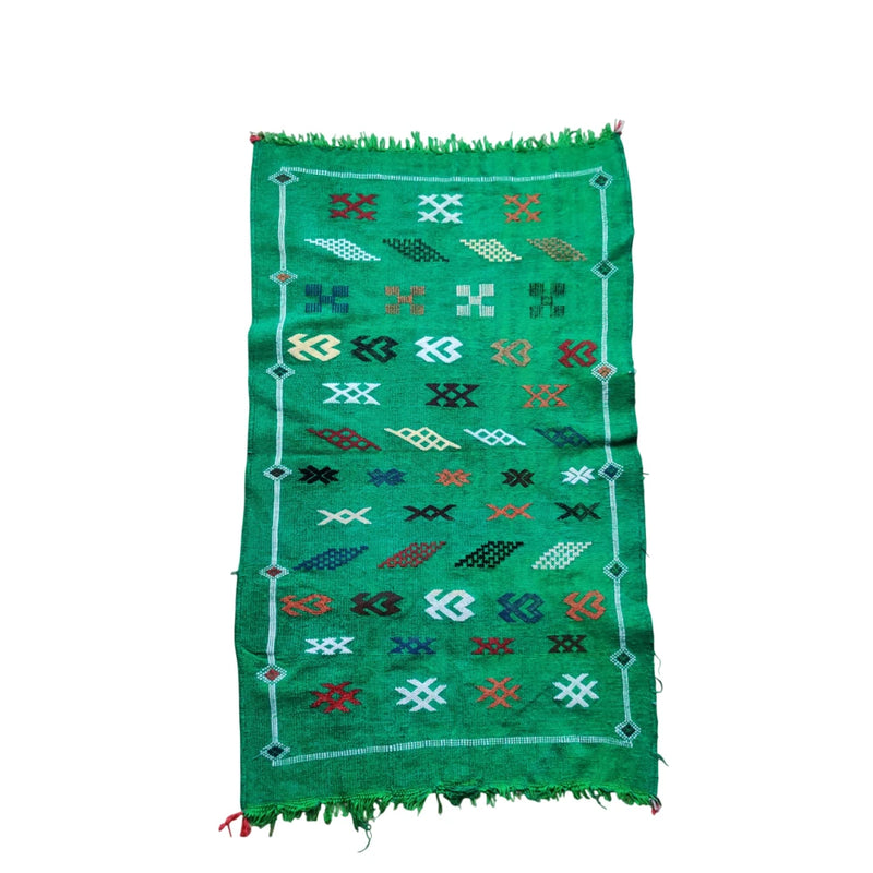 Tapis kilim berbère vert à motifs géométriques colorés et franges aux extrémités.