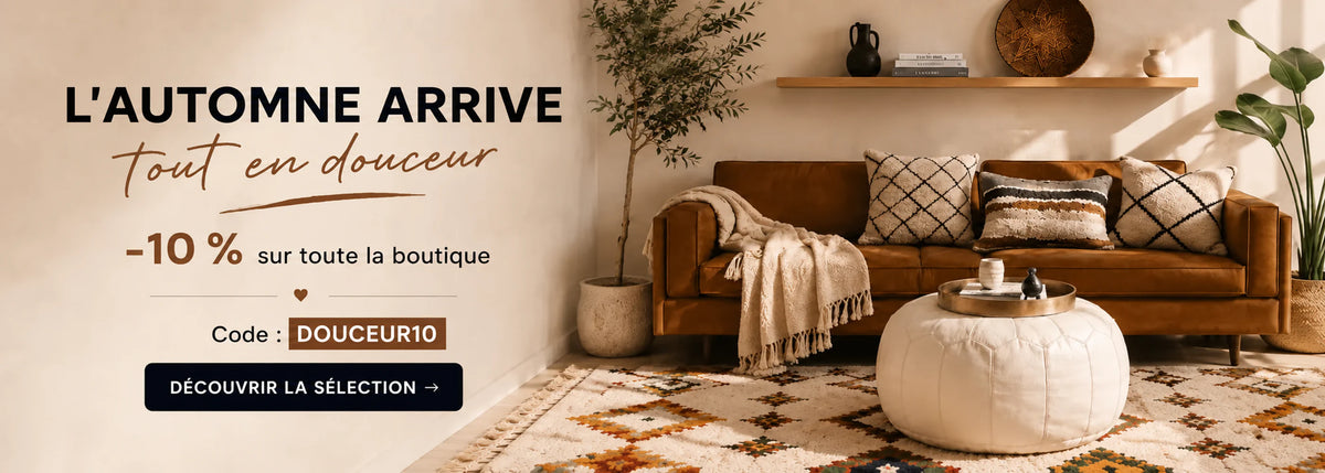 salon avec un canapé et des coussins berbères, on voit un tapis azilal et un pouf blanc