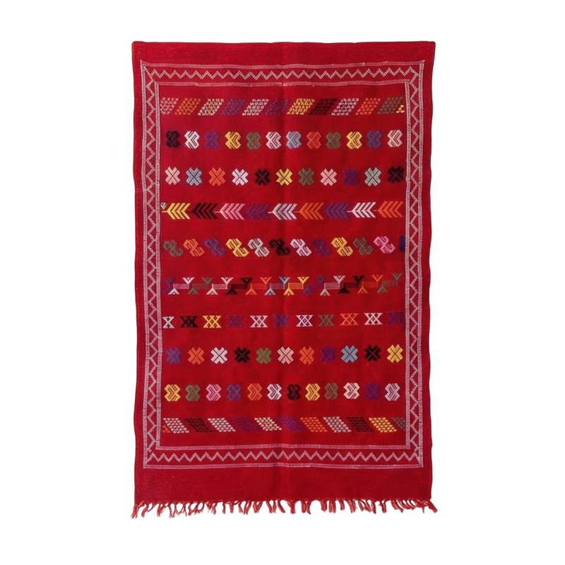 Petit tapis berbère rouge parsemé de motifs ethniques colorés et bordure à franges.