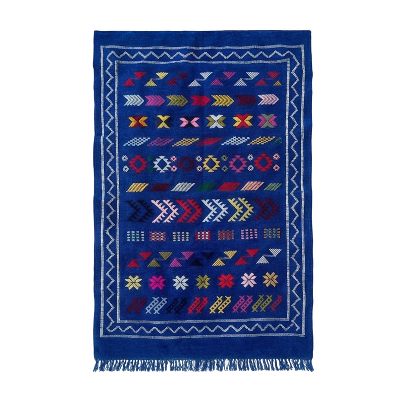 Petit tapis marocain bleu en Sabra, avec motifs géométriques multicolores et bordure blanche.