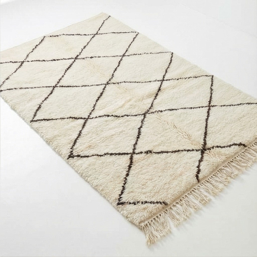 Tapis berbère blanc à motifs losanges noirs, de texture épaisse avec des franges décoratives.