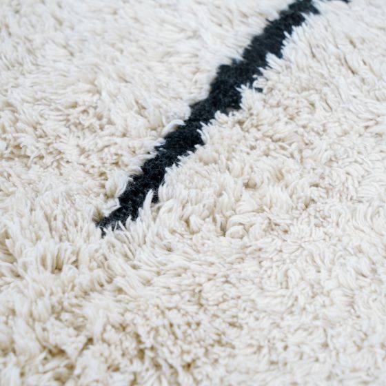Tapis style berbère géométrique en coton crème avec une ligne noire, texture shaggy et douce.