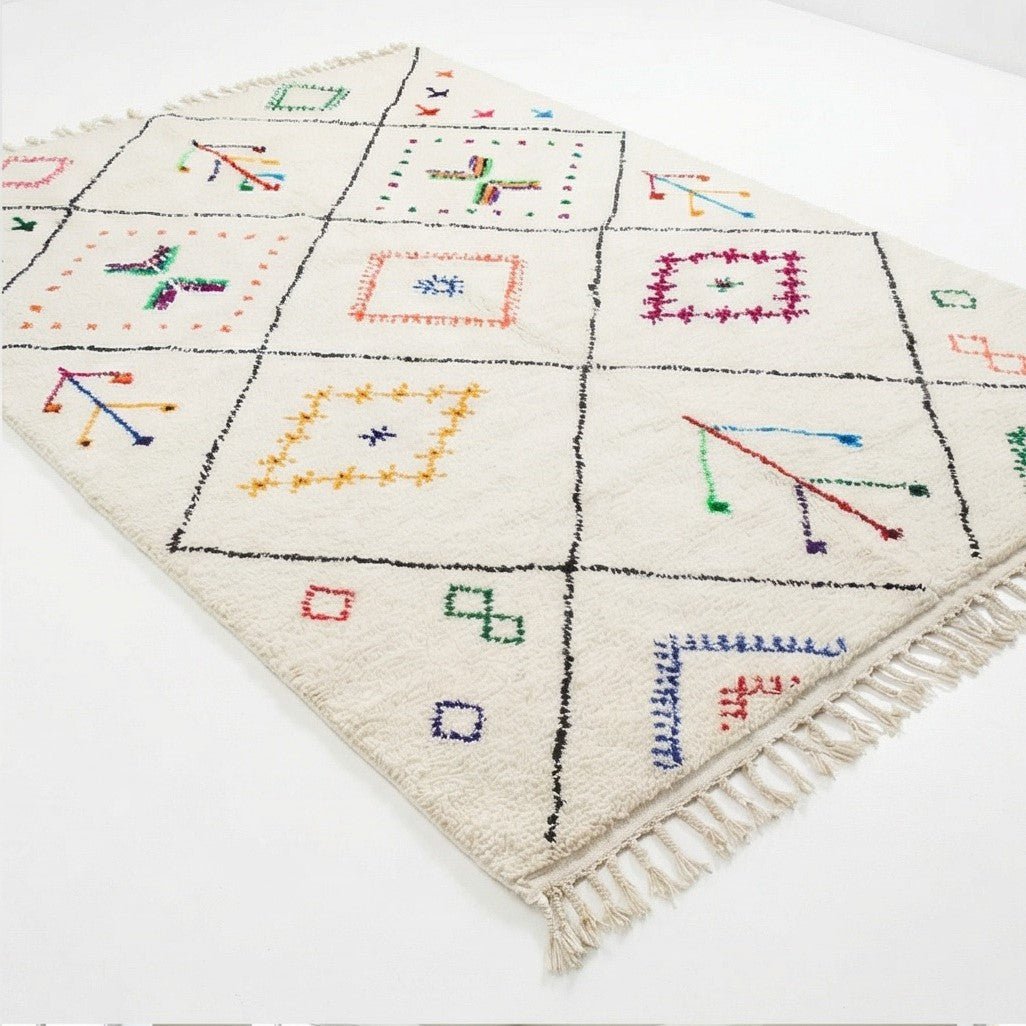 Tapis aux motifs berbères colorés et géométriques, sur fond crème avec franges visibles.