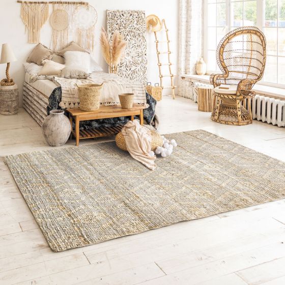 Tapis tressé en jute beige et gris avec motifs losanges, posé sur un plancher en bois clair dans une chambre.