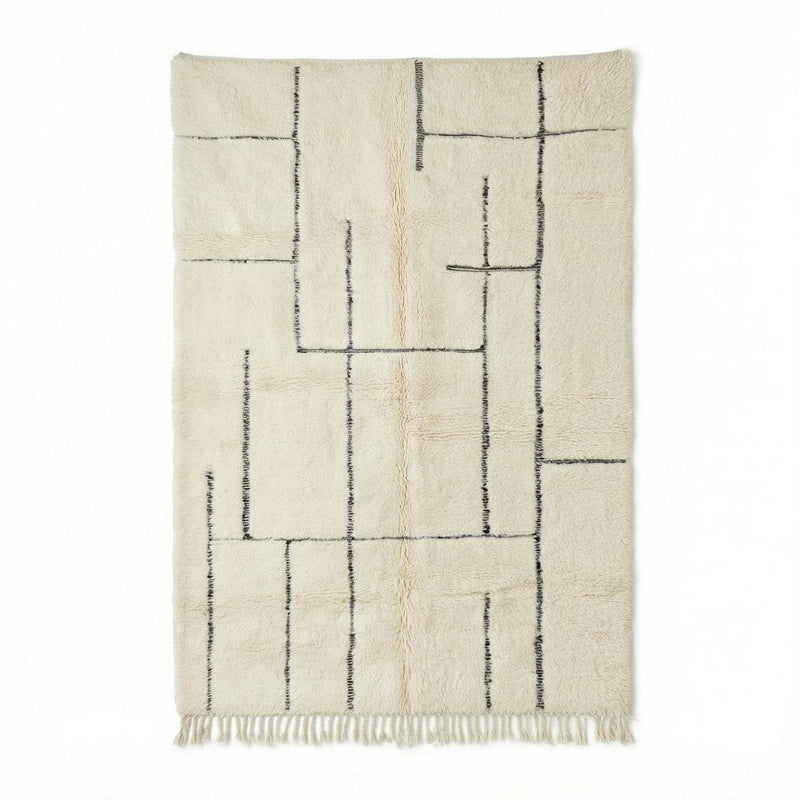Grand tapis berbère graphique ivoire, à motifs géométriques noirs et franges décoratives.
