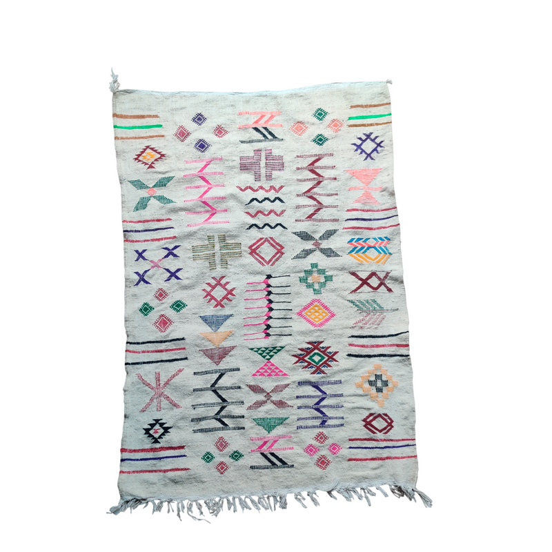 Tapis kilim blanc à motifs berbères de style ethnique, avec des losanges, des croix et des symboles géométriques colorés.
