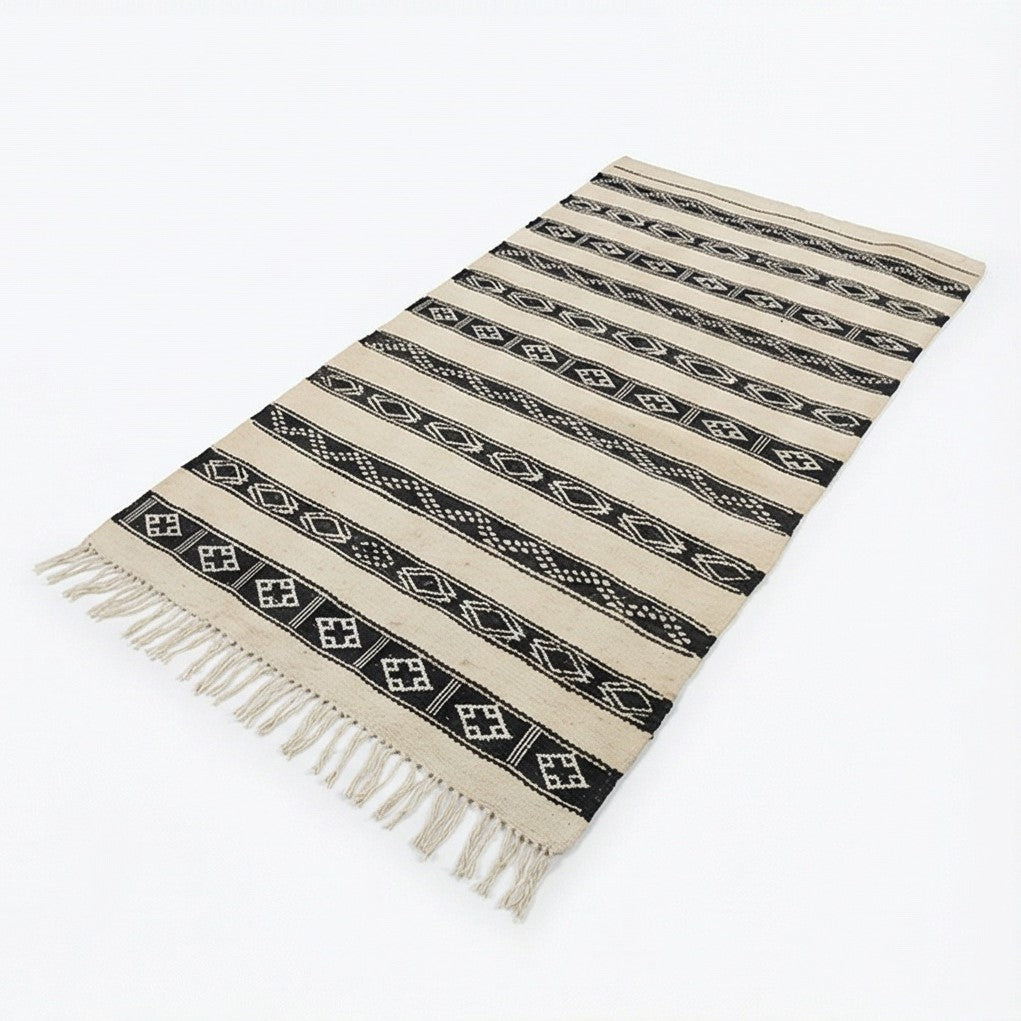 Petit tapis Kilim blanc et noir, de style ethnique, avec motifs géométriques et franges décoratives.
