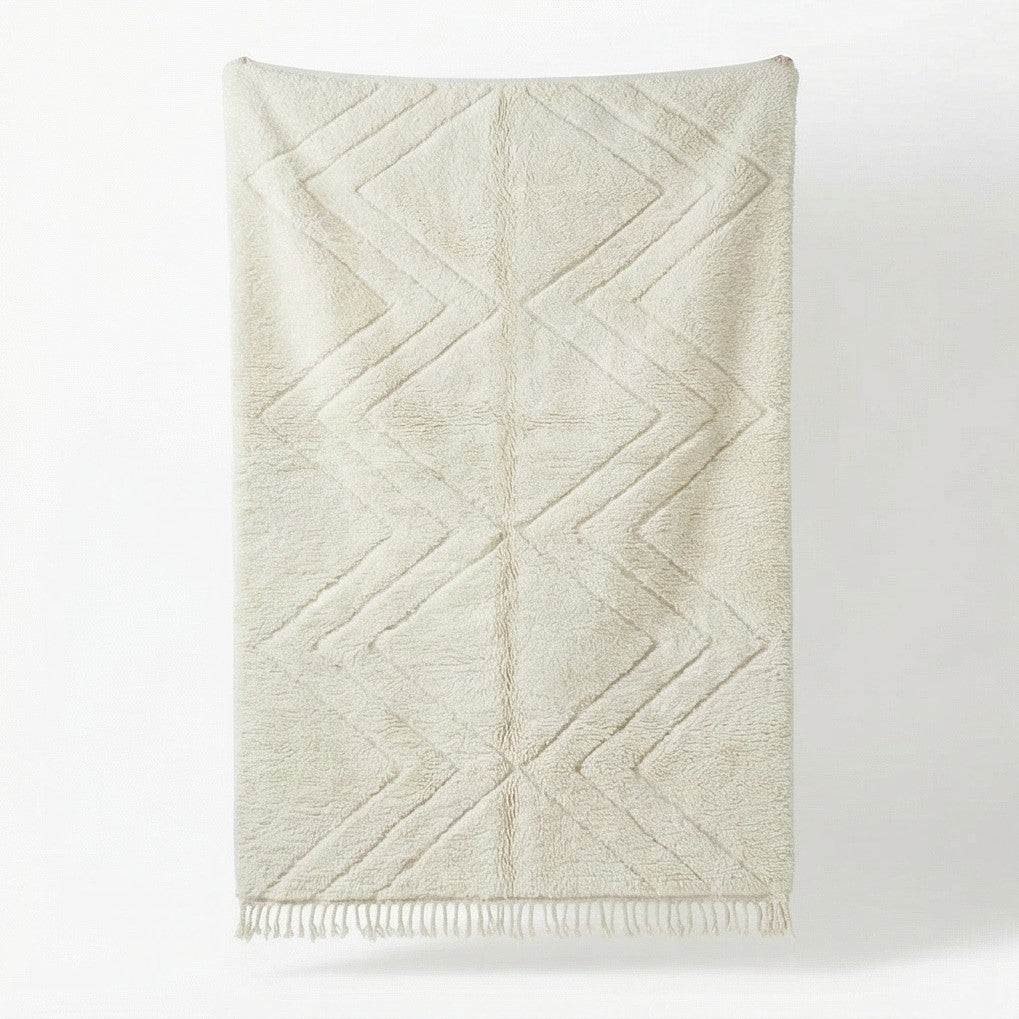 Grand tapis marocain blanc parsemé de motifs en zigzag, avec des franges décoratives sur le bord inférieur.
