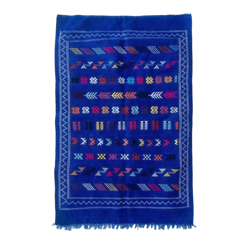 Petit tapis berbère bleu de motifs géométriques multicolores, avec une bordure décorative à chevrons.

