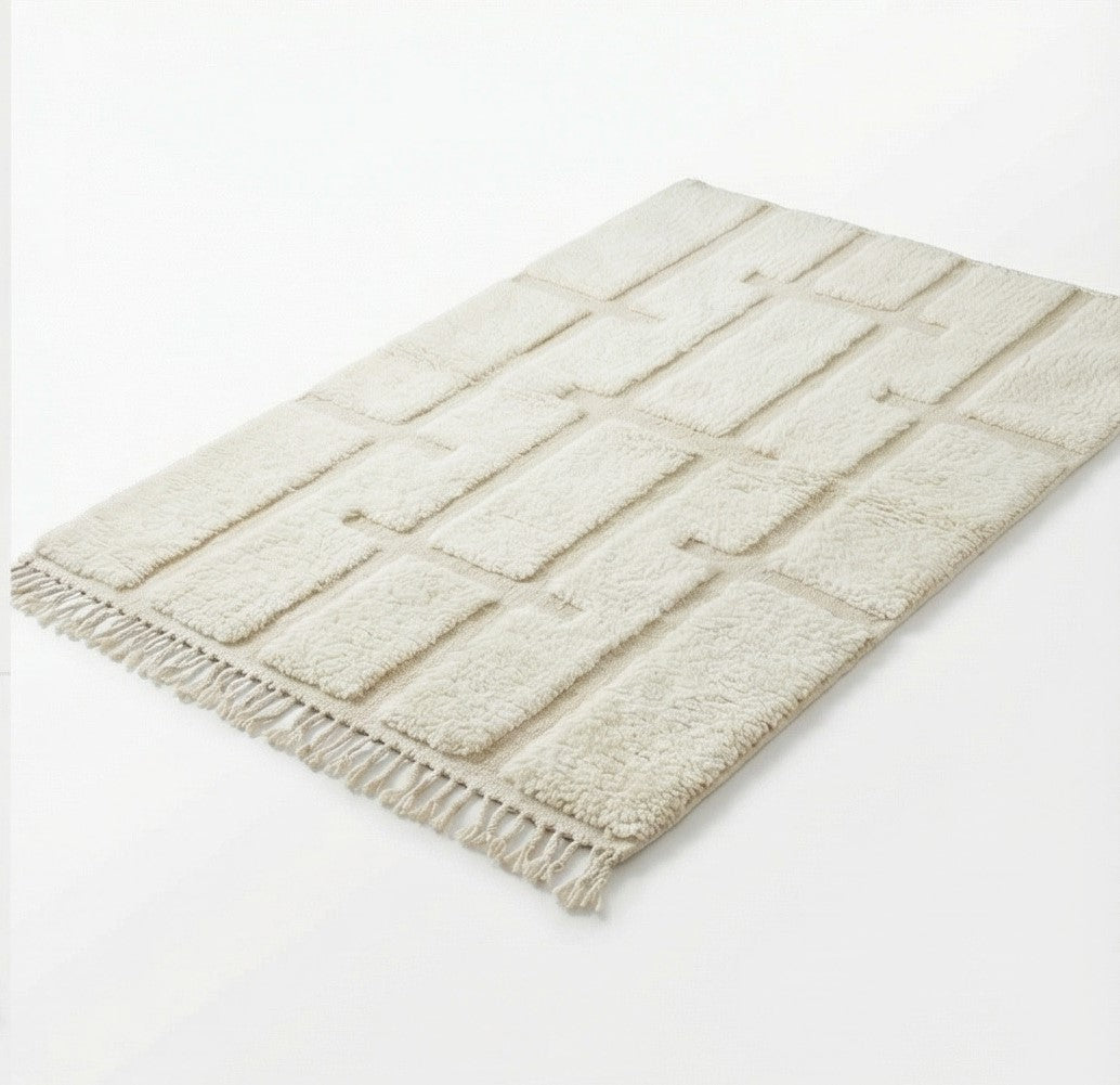 Tapis berbère blanc à motif graphique parsemé de franges décoratives.
