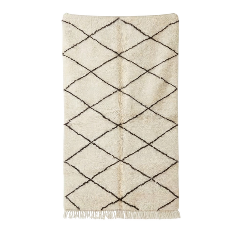 Tapis berbère blanc à motifs losanges noirs, de texture épaisse et franges décoratives.