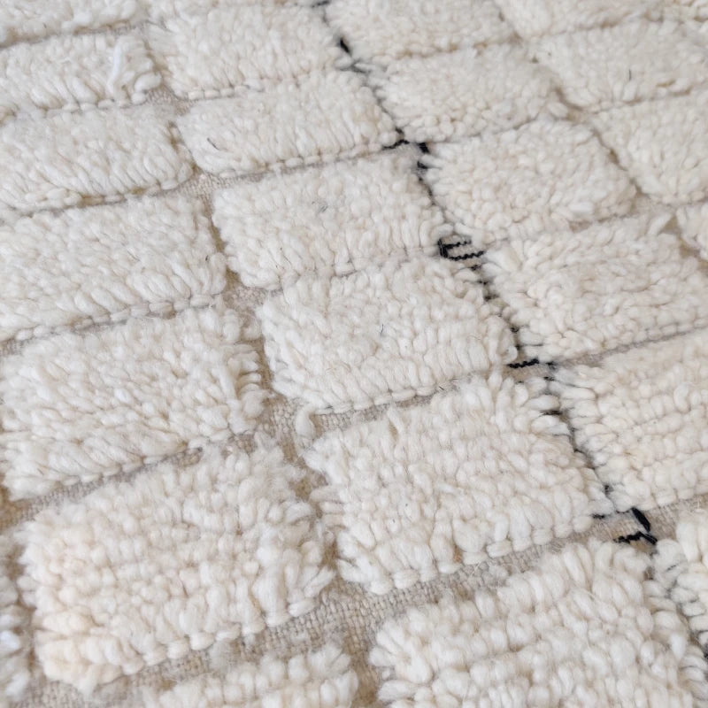 Détail du tissage artisanal du tapis berbère mettant en avant les carreaux blancs précis