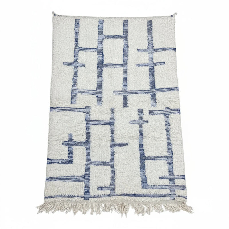 Tapis berbère graphique bleu de style géométrique avec motifs linéaires bleus sur fond blanc cassé, orné de franges.
