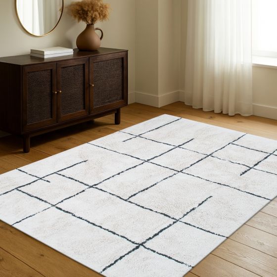 Tapis géométrique style berbère en coton, crème avec des lignes noires irrégulières, posé sur un parquet.