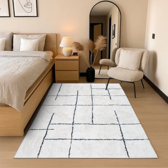 Tapis en coton style berbère géométrique, blanc avec motifs quadrillés noirs irréguliers, dans une chambre aux tons neutres.