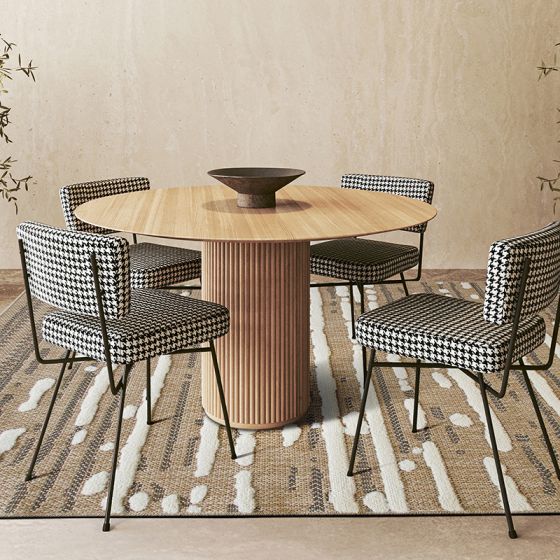 Tapis en jute blanc et noir avec un motif abstrait en relief, placé sous une table à manger en bois et des chaises pied-de-poule.