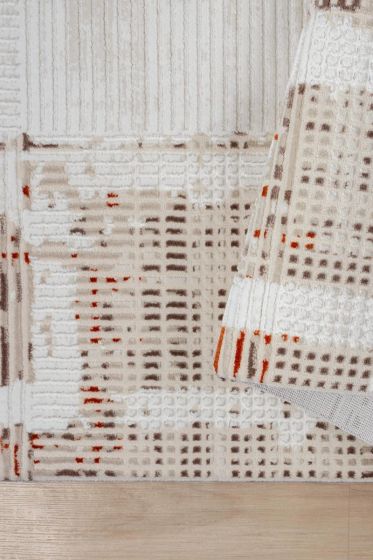 Tapis style berbère à poils ras crème, beige, marron et orange brûlé, avec motifs géométriques abstraits, partiellement replié.
