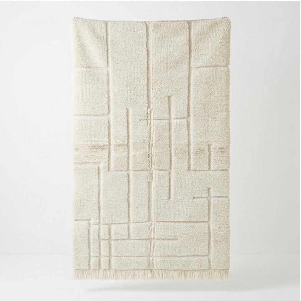 Tapis berbère graphique blanc, de style moderne, avec un motif géométrique en relief et des franges courtes.
