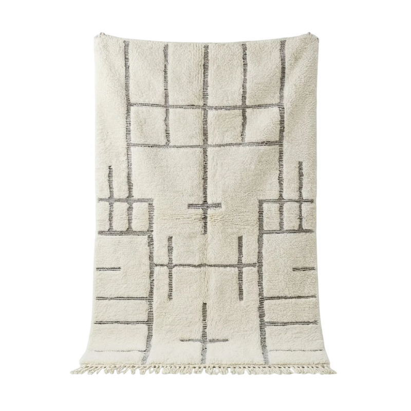Tapis marocain graphique blanc cassé Aman, à motif géométrique noir et franges décoratives.
