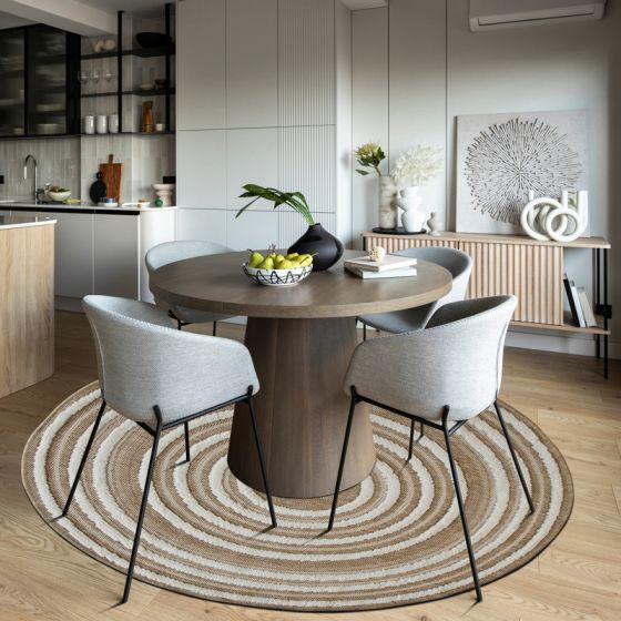 Tapis rond en jute naturel beige à rayures concentriques claires, sous une table à manger.