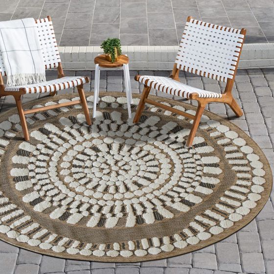 Tapis rond en jute avec motifs blancs en relief concentriques sur un patio gris.